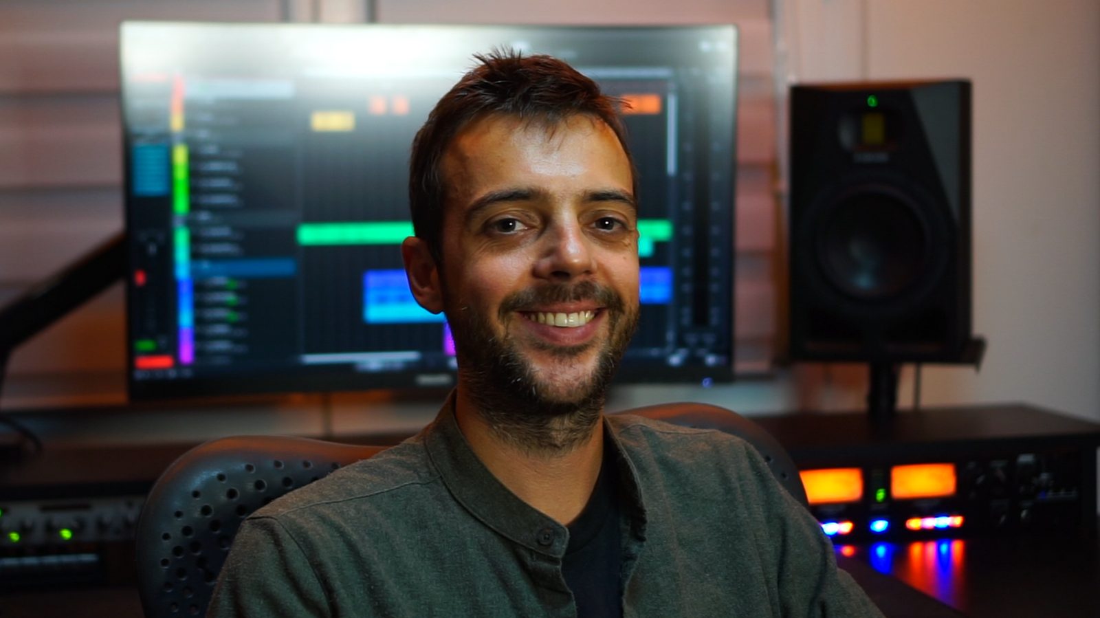 David smiling at his desk, a Reaper session on the screen behind him and studio monitors on the side.